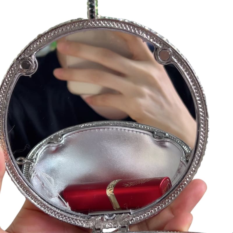 Ornate silver compact mirror reflecting a hand and containing a red lipstick.