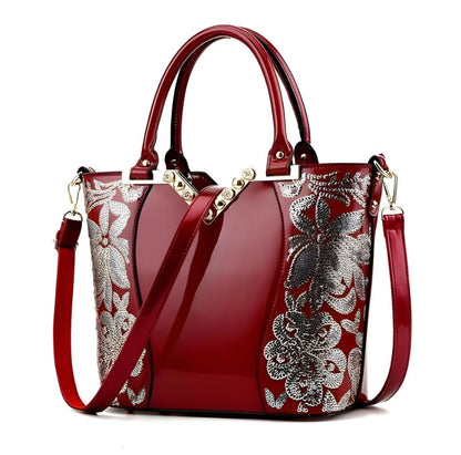 Elegant red handbag with silver floral embroidery and dual handles.