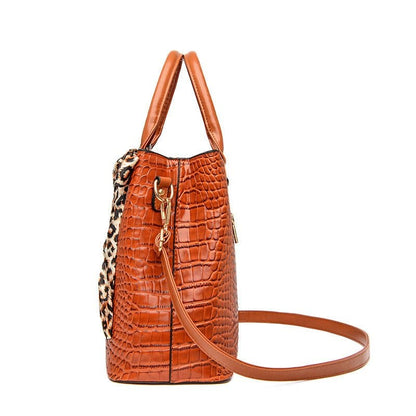 Orange crocodile-textured leather handbag with leopard print accent and detachable shoulder strap.