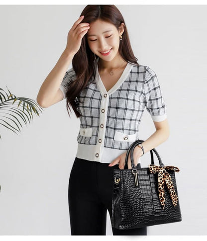 Woman wearing a plaid short-sleeved cardigan and holding a black handbag.