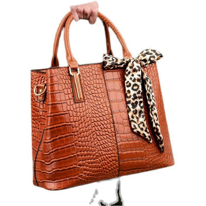 Orange crocodile-textured handbag with leopard print scarf accent.