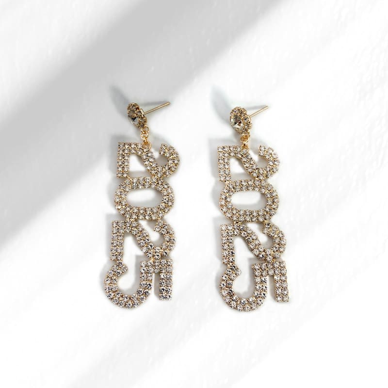 Pair of ornate, dangling earrings with ’BOSS’ spelled out in rhinestones.