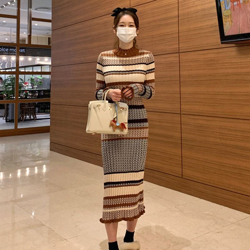 Woman wearing a patterned knit dress and face mask, holding a light-colored handbag.