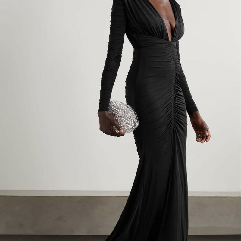 Long black evening gown with a plunging neckline, ruched detailing, and long sleeves.