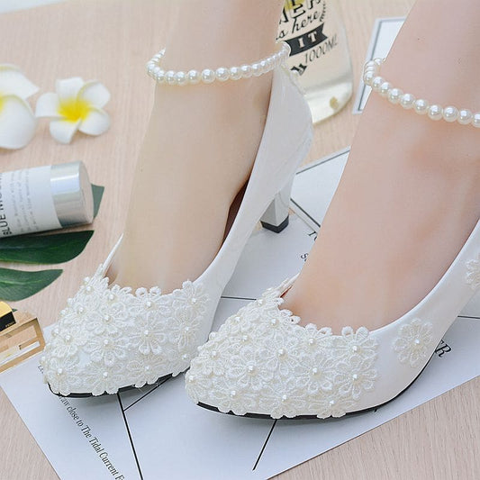 White lace-adorned bridal shoes with pearl-like embellishments and low heels.