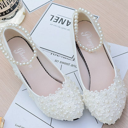 Pair of white, pearl-embellished flat shoes with delicate floral detailing.