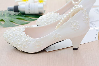 Elegant white bridal shoes with pearl-like embellishments and low heels.