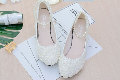 Pair of white lace bridal shoes adorned with pearls.