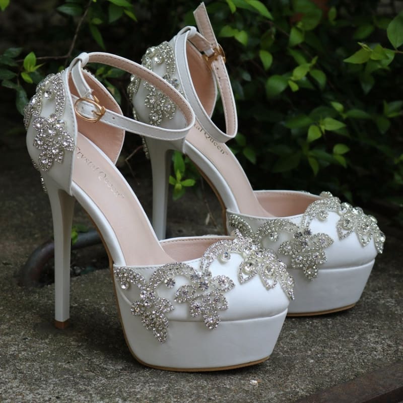 Ornate white high-heeled platform sandals adorned with crystal embellishments.