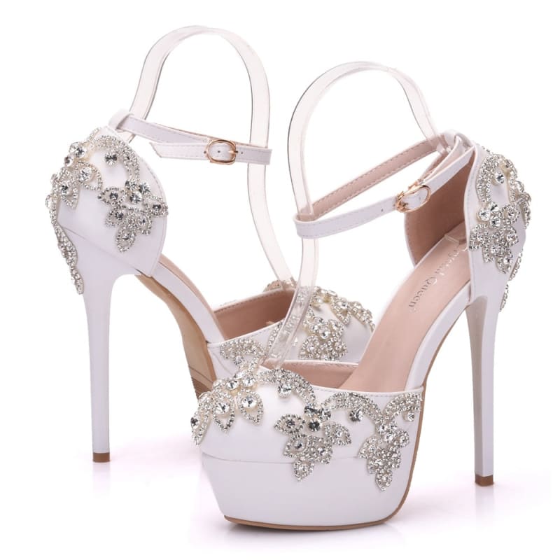 Ornate white high-heeled platform shoes with crystal embellishments and ankle straps.