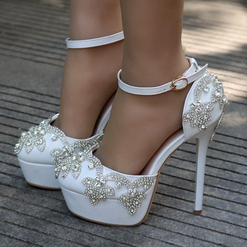 Ornate white high-heeled platform shoes with crystal embellishments and ankle straps.