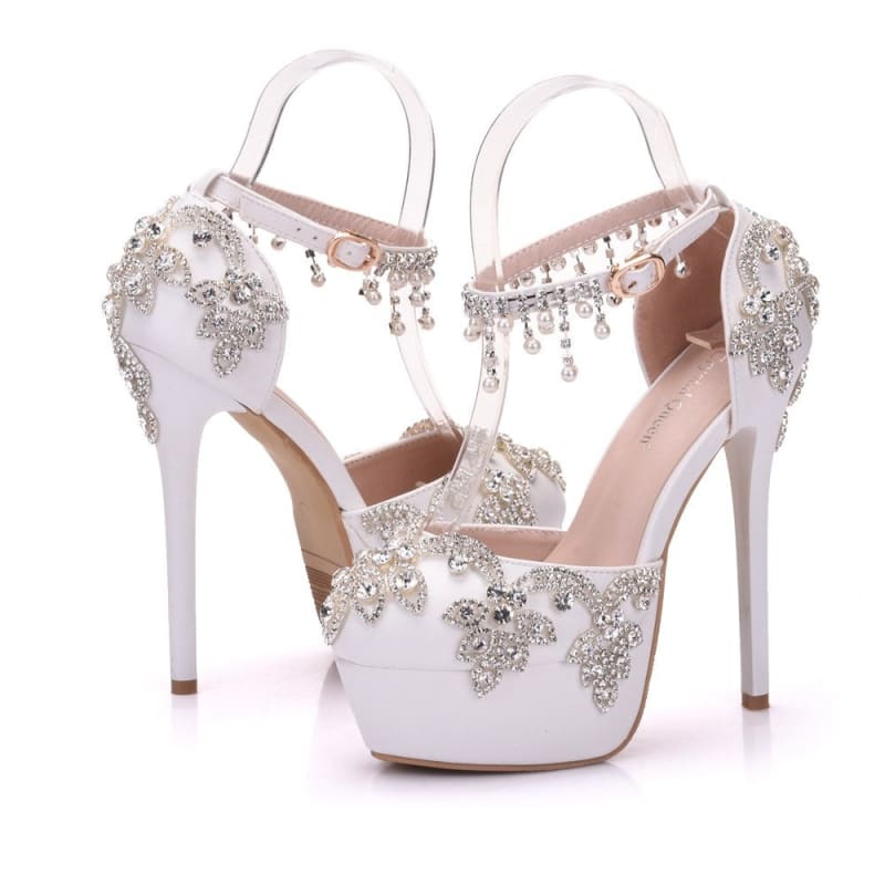 Ornate white high-heeled platform sandals adorned with crystal embellishments and dangling jewels.