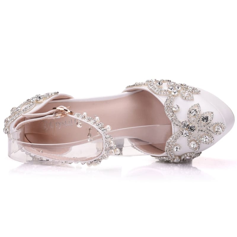 Ornate white satin bridal shoes adorned with crystal embellishments and floral designs.