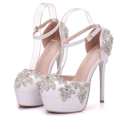 Ornate white high-heeled platform shoes with crystal embellishments and ankle straps.