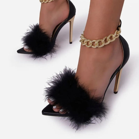 Pair of black high-heeled sandals with fluffy fur straps and gold ankle chains.