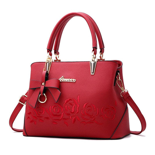 Red leather handbag with embossed rose design and gold-tone hardware.