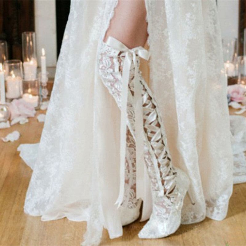 Pair of white lace-up knee-high boots with a floral lace pattern.